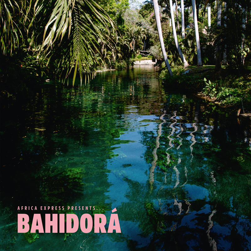 The album cover for Africa Express Presents... Bahidorá features a lush, tropical scene with crystal-clear water reflecting palm trees and dense greenery. The title appears in bold pink letters at the bottom left,