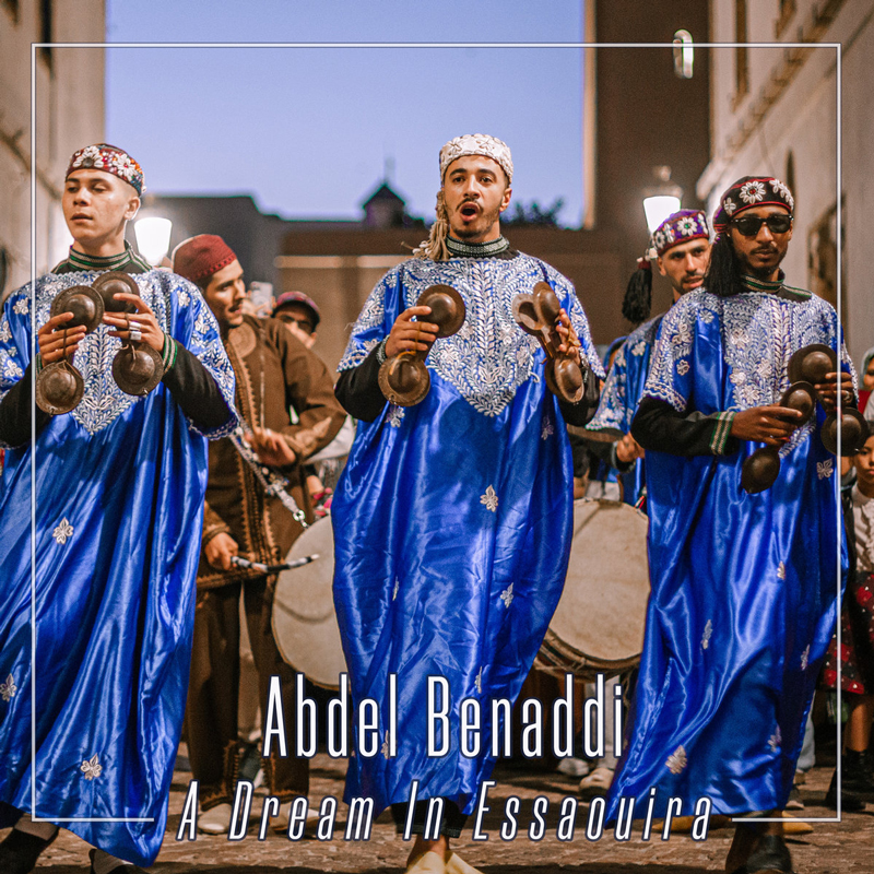 Abdel Benaddi — A Dream In Essaouira cover artwork. Gnawa musicians wearing blue robes and playing karkabas marching down a street, followed by drummers.