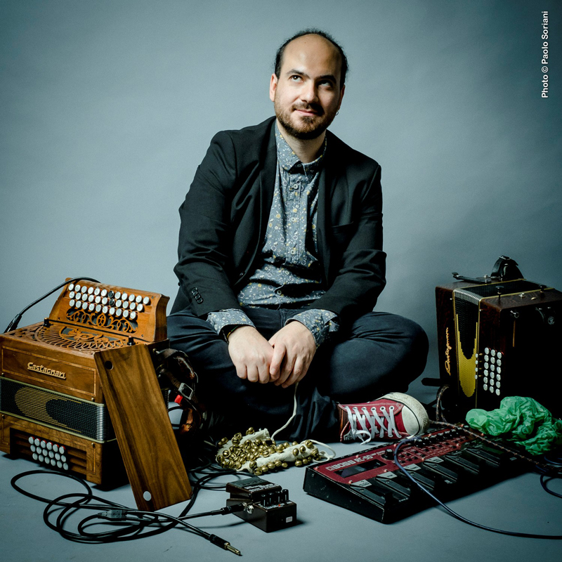 Alessandro DAlessandro - Photo by Paolo Soriani. The artist sitting next to an accordion and electronic effect devices.