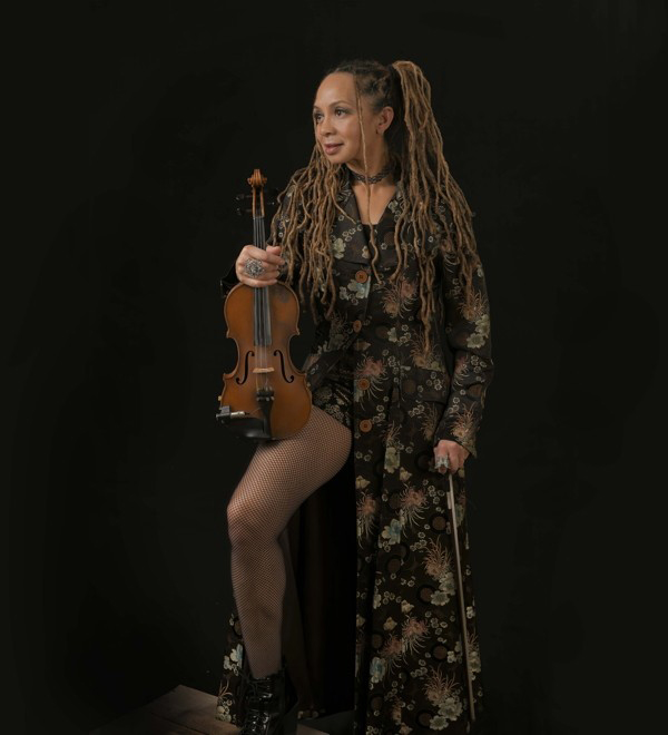 Anne Harris wearing a dress, standing, holding a violin.