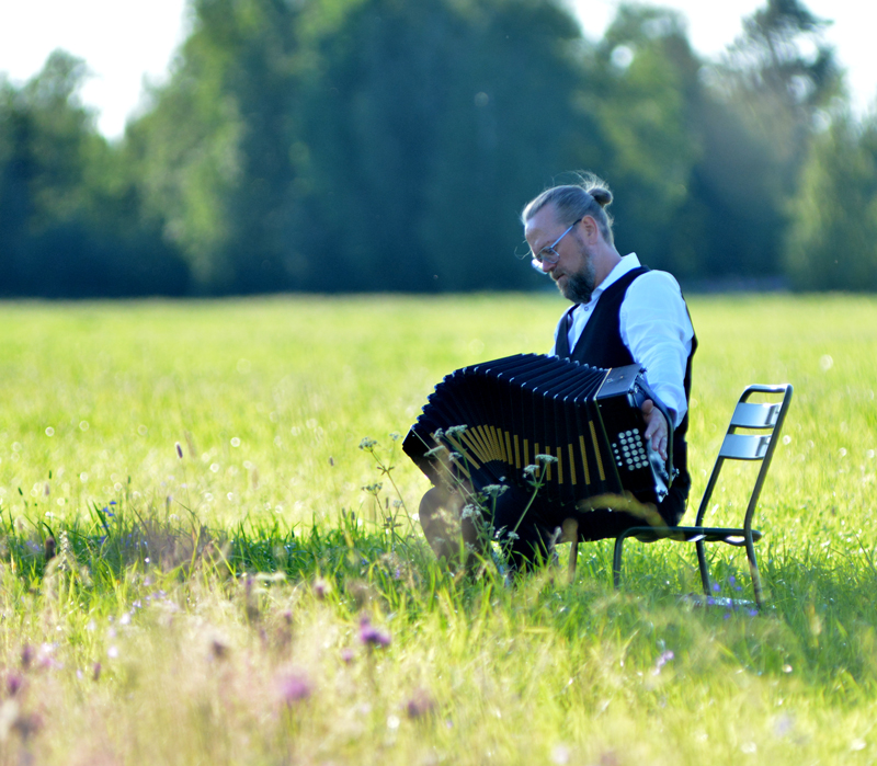 Antti Paalanen - Photo by Kimmo Kansala. Paalanen playing accordion in a field.