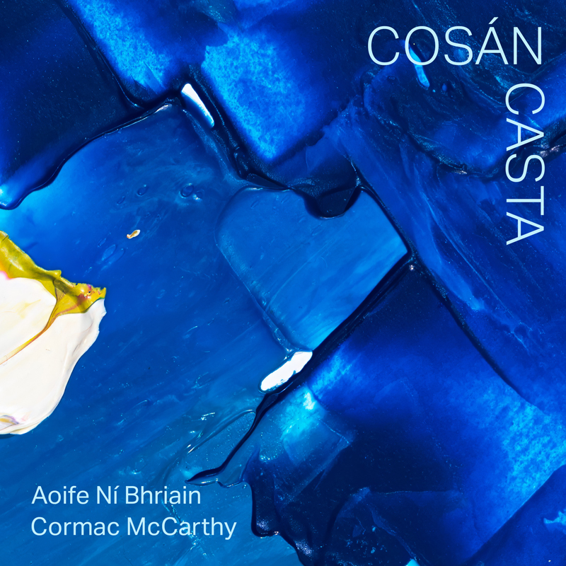 The cover features luminous blues that resemble layered glass or melting ice. The title “Cosán Casta” appears vertically along the right edge in white lettering, while the artists’ names—Aoife Ní Bhriain and Cormac McCarthy—sit discreetly in the lower left.