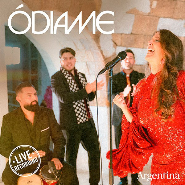 Argentina - Ódiame single cover. Argentina wearing a red dress standing by a microphone, surrounded by three musicans.