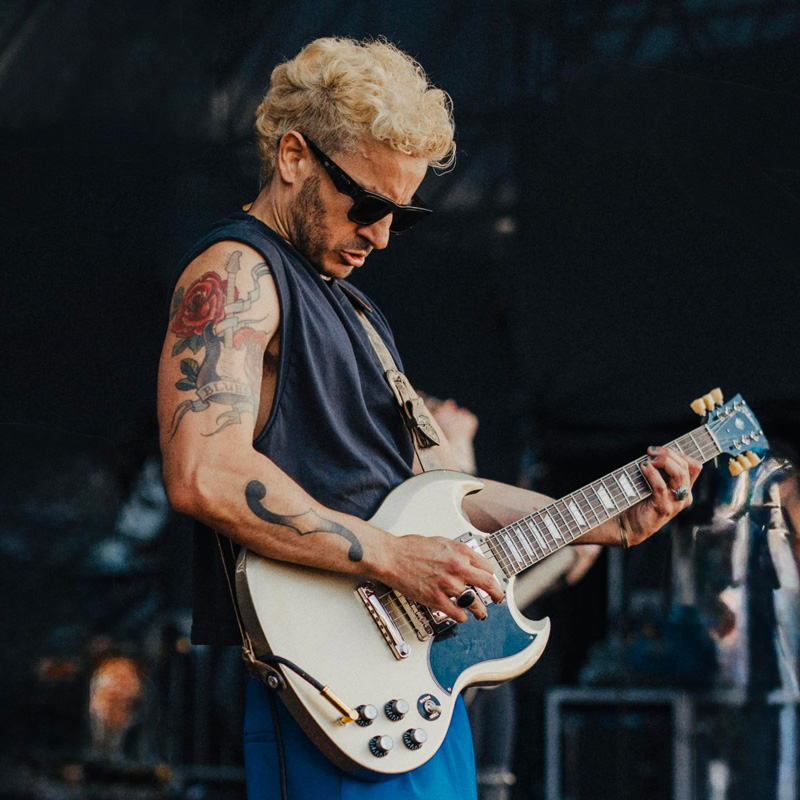 Artur Menezes playing electric guitar live, wearing sunglasses.
