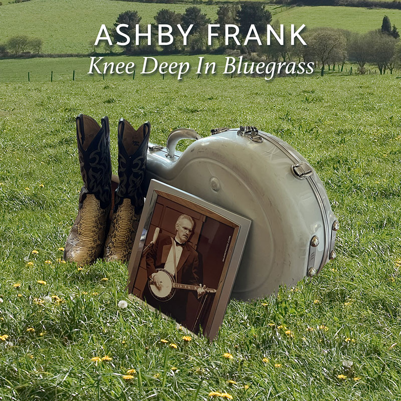 Ashby Frank - Knee Deep In Bluegrass cover artwork. a grass field with a memorial including a photo of Terry Baucom, a pair of cowboy boots and a banjo case.