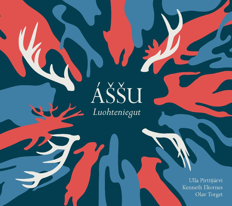 The album cover for Áššu – Luohte­niegut features stylized silhouettes of reindeer and antlers in red, white, and blue, radiating outward in a circular pattern against a dark teal background. The typography is clean and centered, with the artists’ names—Ulla Pirttijärvi, Kenneth Ekornes, and Olav Torget—listed discreetly in the lower right corner.