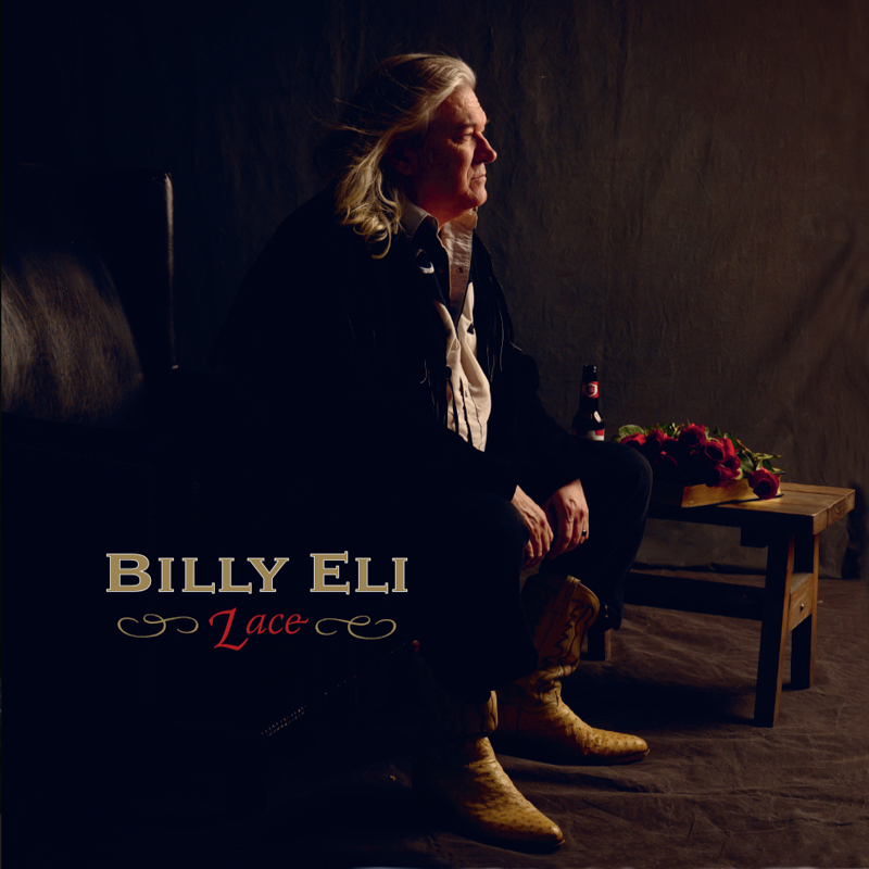 The album cover for Lace by Billy Eli features the artist seated in a dimly lit room, gazing thoughtfully into the distance. He wears a fringed jacket and yellow cowboy boots, with a bottle of beer beside him on a rustic wooden table topped with red roses.