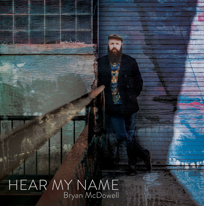 The cover for Hear My Name by Bryan McDowell features an urban backdrop with weathered wood, metal, and faded paint. Bryan McDowell stands against a wall in a dark coat and cap. The title and artist name appear in clean, white text at the bottom.