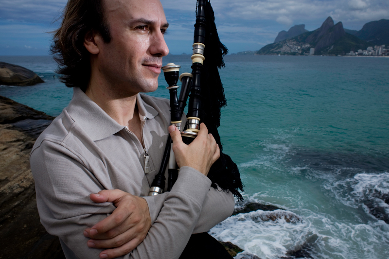 piper Carlos Núñez holding his bagpipe to the heart. He is standing by the seashore.