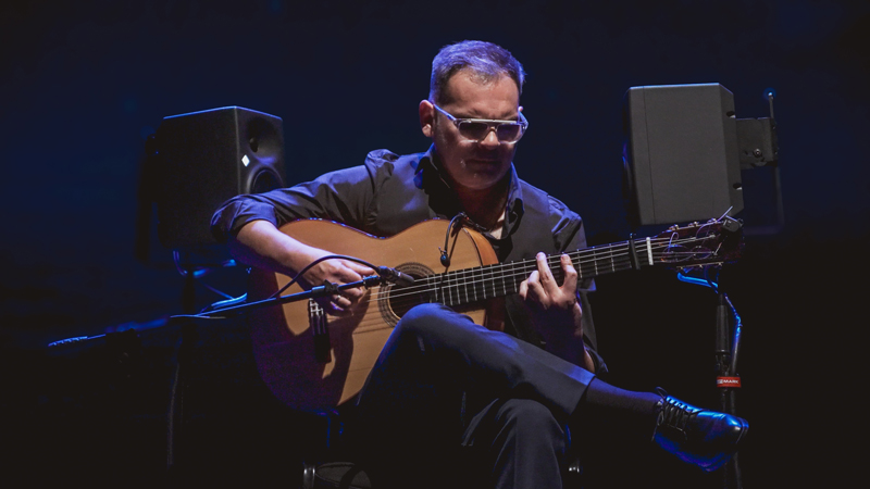 Chico Gallardo playing guitar, wearing eyeglasses.