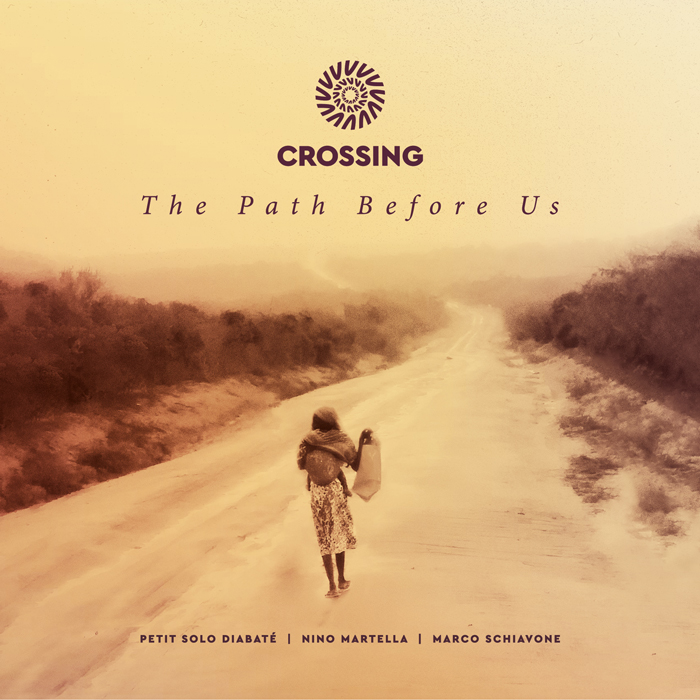 A lone figure walks along a dusty road that disappears into a hazy horizon. Warm sepia tones dominate the scene, giving it a reflective atmosphere. The album title The Path Before Us sits in elegant script beneath the word “Crossing,” with the artists’ names listed at the bottom. The imagery suggests journey, distance, and quiet persistence.