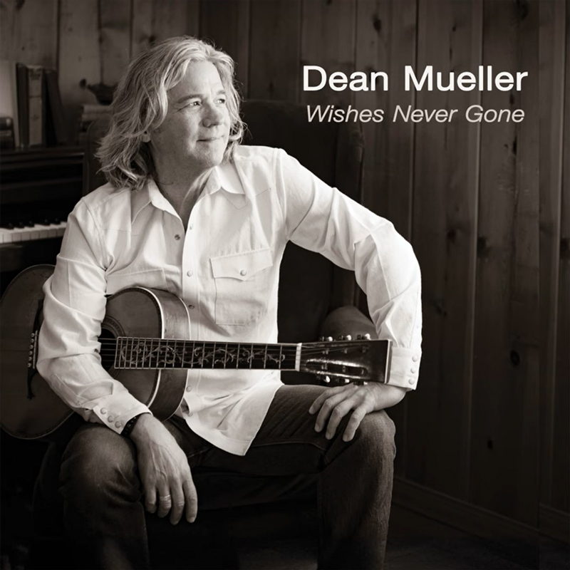 Dean Mueller - Wishes Never Gone. A photo of Dean sitting, holding a guitar under his arm.