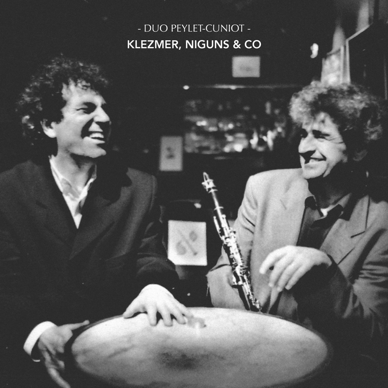 Duo Peylet-Cuniot - Klezmer, niguns & co cover artwork. a nlack and white photo of the two artists sitting around a table smiling.