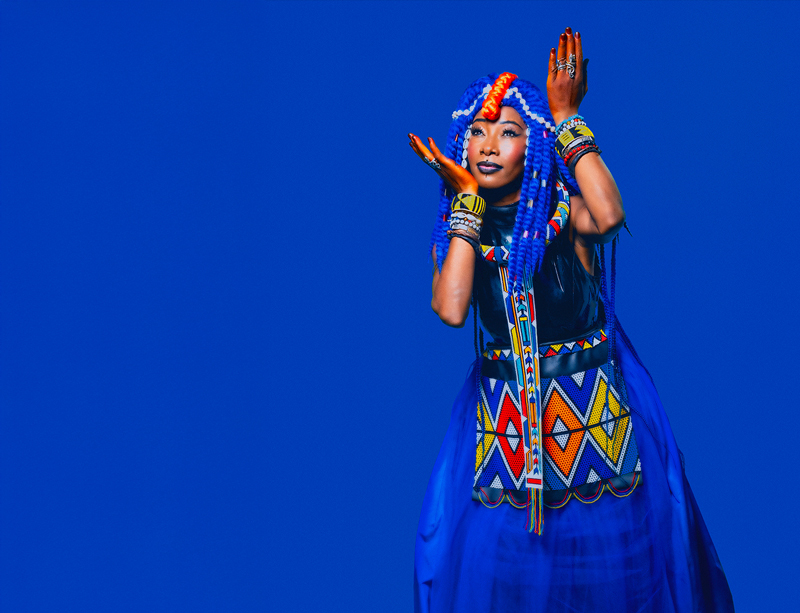 Fatoumata Diawara wearing a blue traditional dress over a blue background.