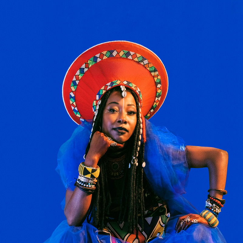 Fatoumata Diawara — Photo by Marcello Perego. Fatoumaa wearing a blue dress and a traditonal red headdress.