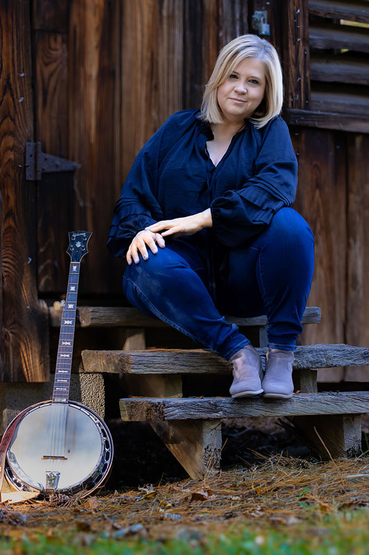 Gena Britt. Photo by Laci Mack. Gena sitting on steps next to a banjo.