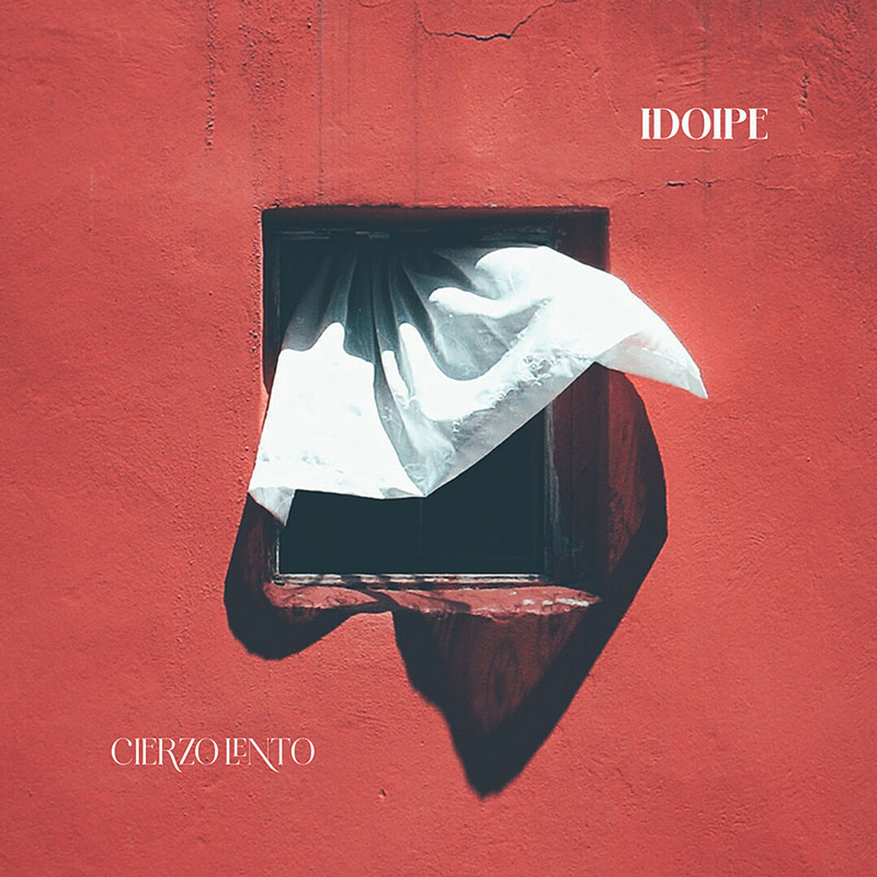 The album cover for Cierzo Lento by Idoipe features a photograph of a white curtain billowing out of a small window set in a vivid red wall.The artist's name appears in the top right corner, with the album title in the bottom left.