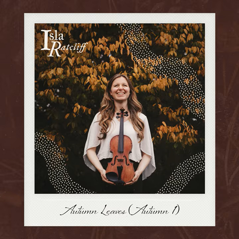 Isla stands outdoors, smiling, before golden autumn foliage, holding a violin at her waist. Her light blouse contrasts with the leaves behind her. The name “Isla Ratcliff” appears in the upper corner, and the handwritten title Autumn Leaves (Autumn I) sits beneath the Polaroid-style frame.
