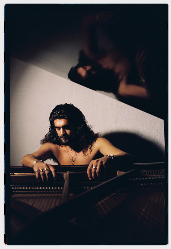 Israel Fernández – Photo by Rufo Reverte. Israel shirtless with his hands on top of a grand piano.