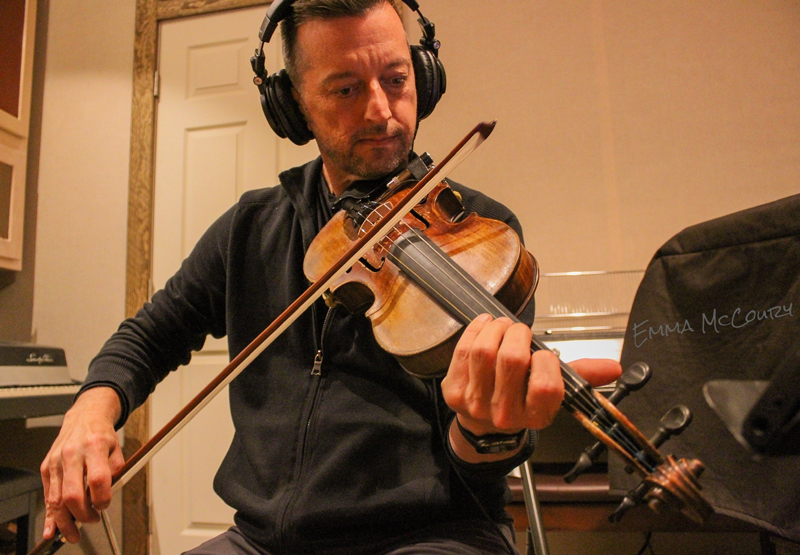 Jason Carter playing fiddle with headphones on.