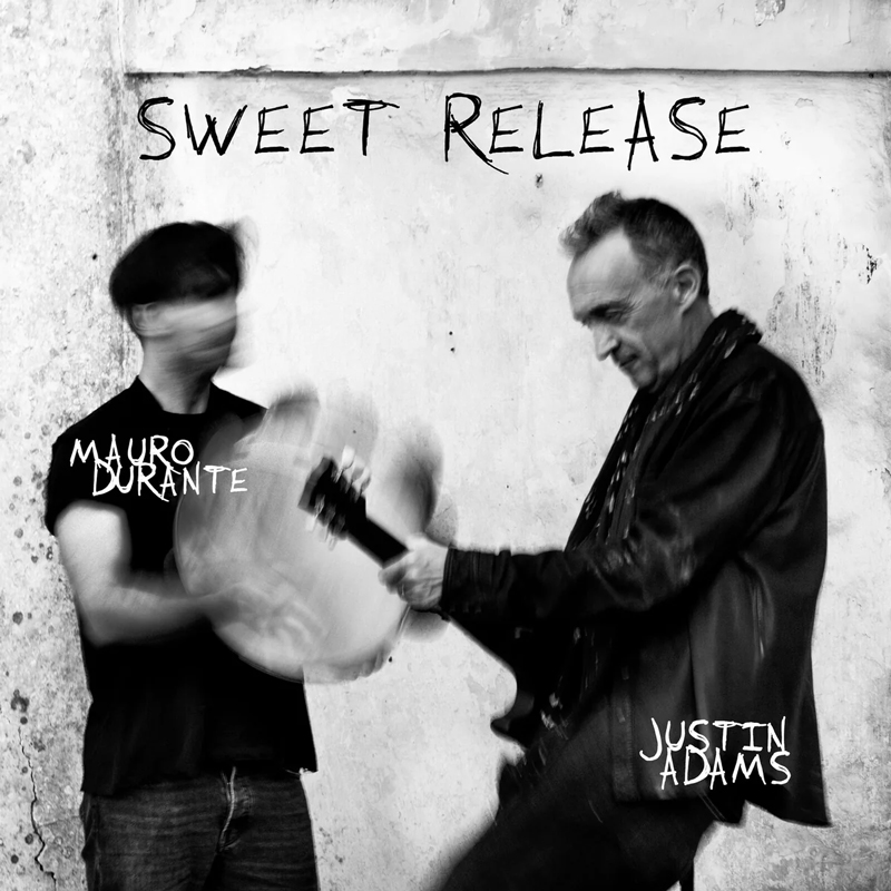 Justin Adams & Mauro Durante - Sweet Release cover artwork. A black and white photo featuin Adams on guitar and a blurry image of Durante playing frame drum.