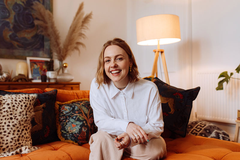 Kim Carnie sitting on a sofa, smiling.