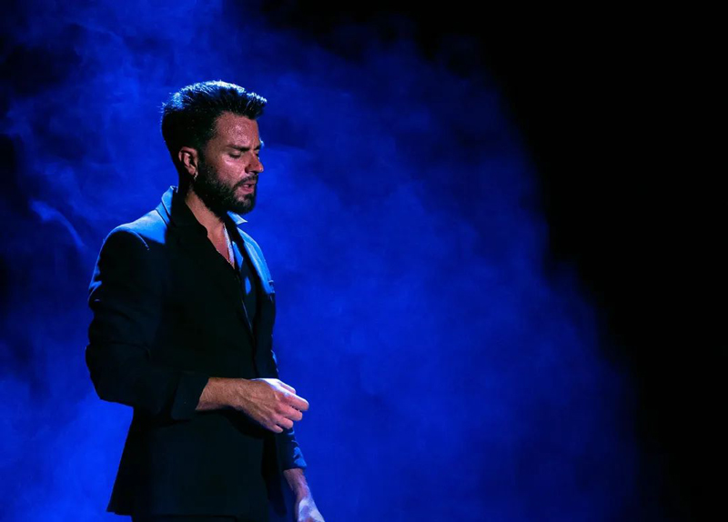 Manuel de Gines standing on stage with blue lighting.