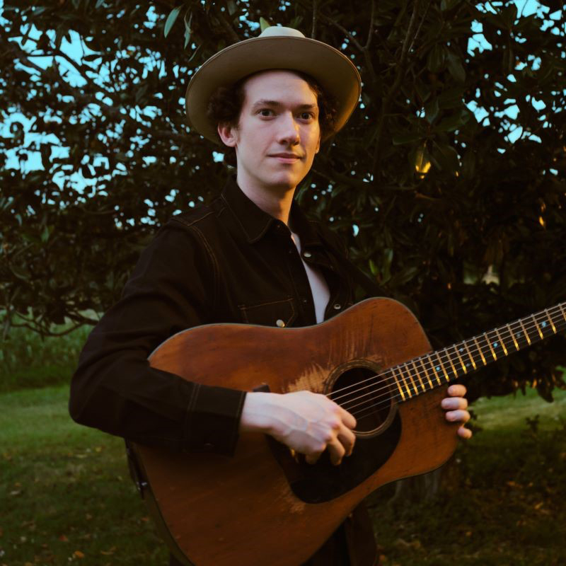 Mason Via playing guitar outdoors wearing a hat