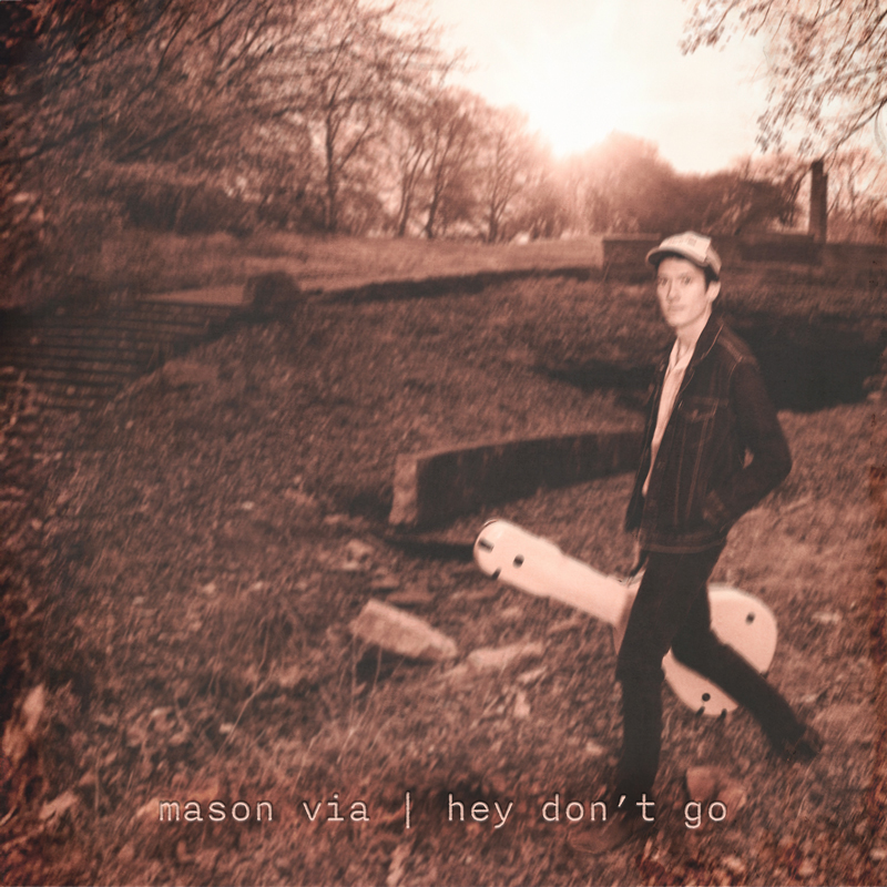 Mason Via - "Hey Don't Go" cover artwork. A photo of the artist walking outdoors carrying a guitar case.