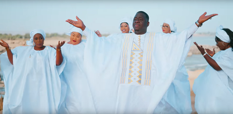 Niarela Papou from his Mali video. Niarela wearing a light blue robe surrounded by female singers.