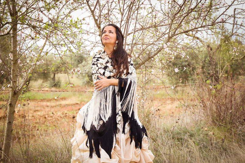Olivia Molina. A photo of the artist wearing a flamenco dress, standing outdoors in a field.