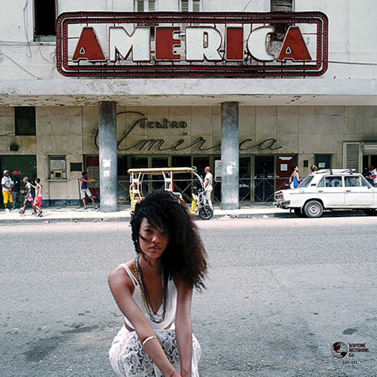 Orquesta Akokán - América cover artwork. A young woman crouches in the foreground of an urban street, gazing directly at the camera. Behind her, the weathered façade of the América Theater features a large vintage marquee spelling “AMERICA.” the cover also features classic cars and pedestrians.