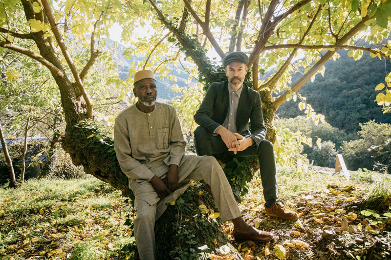 Piers Faccini and Ballaké Sissoko sitting on a tree in the woods