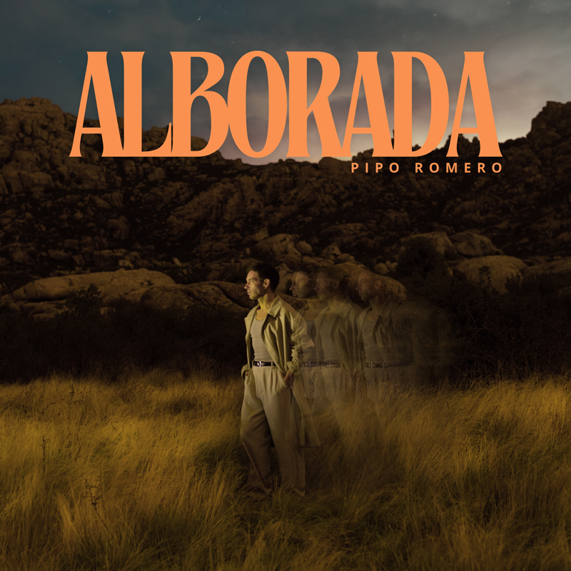 The album cover for Alborada by Pipo Romero features the artist standing in a golden field surrounded by rugged rocks under a dusky sky. He wears a beige trench coat and looks to his left, illuminated by soft, amber light. Multiple faint images of him trail behind. The album title ALBORADA appears in large, bold orange letters across the top, with his name in smaller text below it.