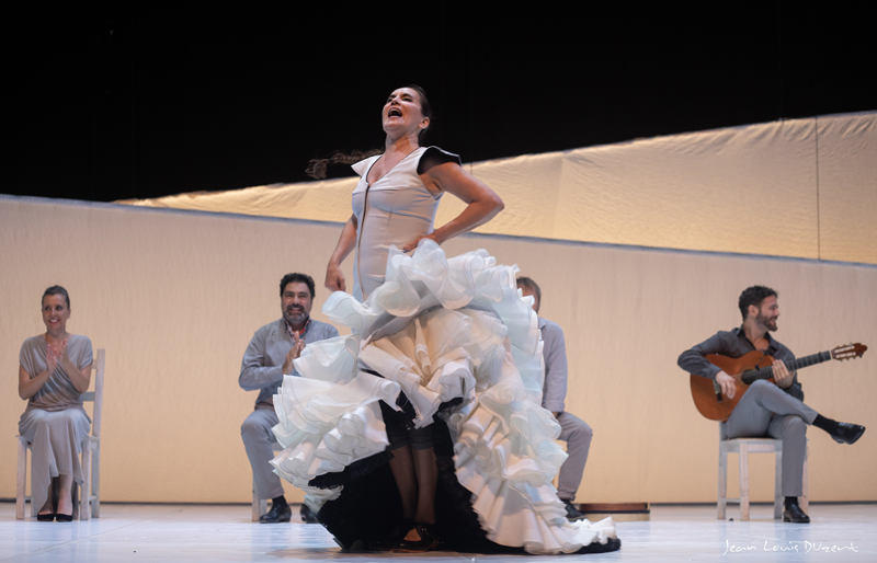 Rafaela Carrasco - photo by Jean-Louis Duzert. Rafaela dancing in a white dress. Musicians sit behind her.
