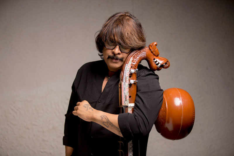 Rajhesh Vaidhya standing, hugging his veena