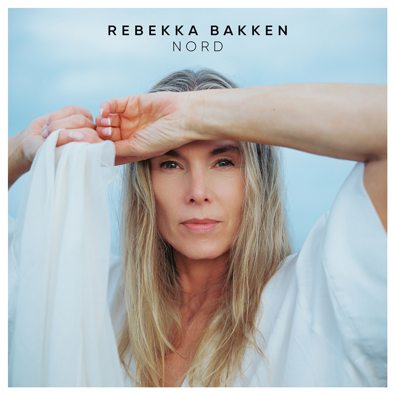 Rebekka Bakken - Nord cover artwork. a photo o Rebekka, a blond woman with long hair, with her arm across her had.