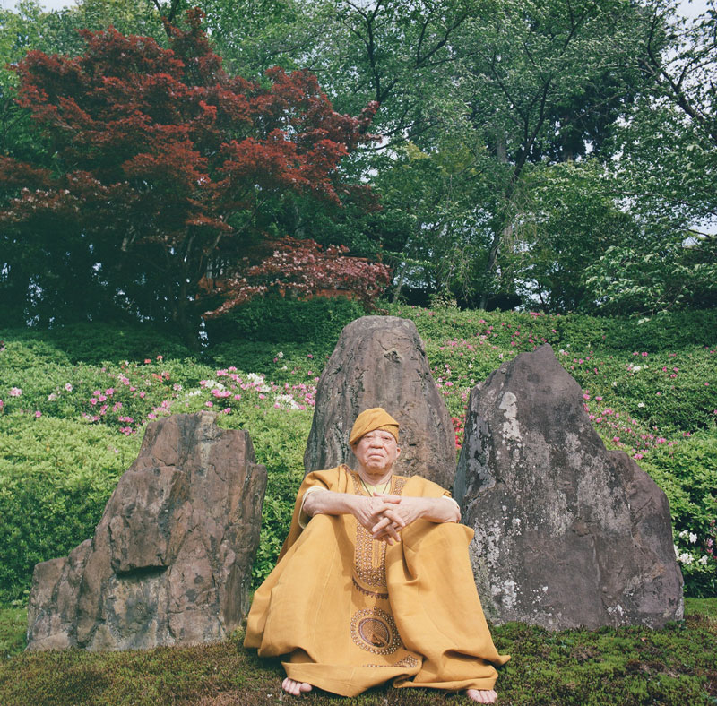 Salif Keita sitting, leaning on a large boulder. Photo by Lucille Reyboz