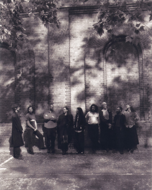Shovel Dance Collective - Photo by Brad Gilbert. Sepia colored photo of the band lined up outdoors by some trees.