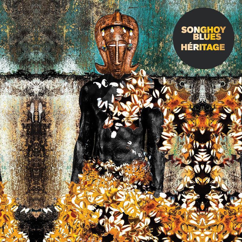 The album cover for Héritage by Songhoy Blues features a central figure with dark, glossy skin wears a traditional African mask adorned with beads. The body is partially covered in cowrie shells and golden-hued organic patterns. The background blends weathered textures with a symmetrical, mirrored design. The album title and band name appear in bold, yellow and white text within a black circle in the upper right corner.