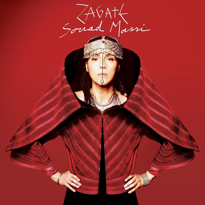 The cover of Zagata by Souad Massi features the artist posed front and center against a red background. She wears an elaborate red garment with wide, wing-like shoulders and intricate patterns, paired with traditional jewelry and a detailed headpiece.