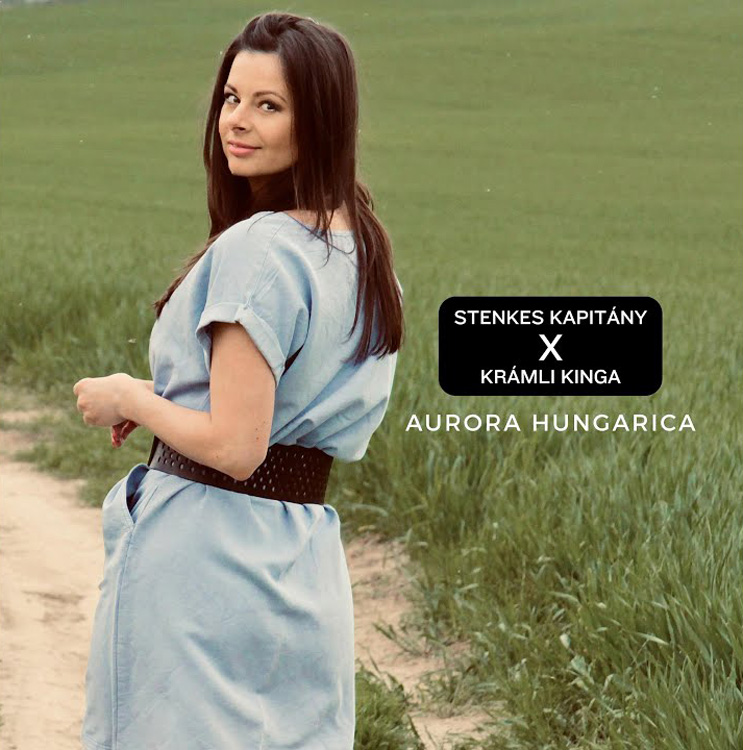 Stenkes Kapitány - Aurora Hungarica cover artwork. The cover of Aurora Hungarica features a woman standing on a rural path beside a green field, looking back toward the camera. She wears a light blue dress with a wide dark belt.