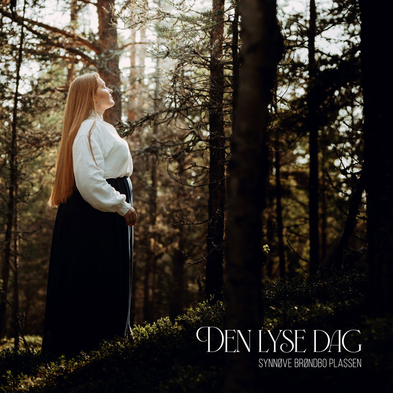 Synnøve Brøndbo Plassen - Den Lyse Dag cover artwork. Synnøve Brøndbo Plassen standing in a forest.