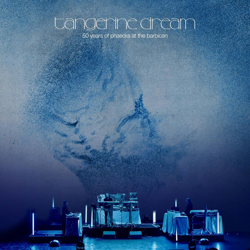 Tangerine Dream - 50 Years Of Phaedra cover artwork. A photo of the concert with blue lighting. The three musicians facing each other and the original album artwork displayed in the background.