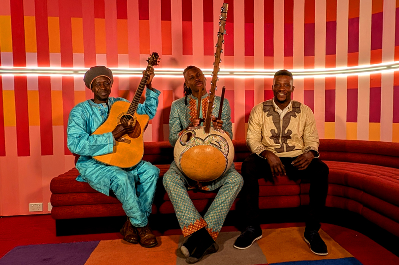 The Mandé Spirit — Photo by Kurt Eckardt. The three artists sitting on a sofa, holding their musical instruments.