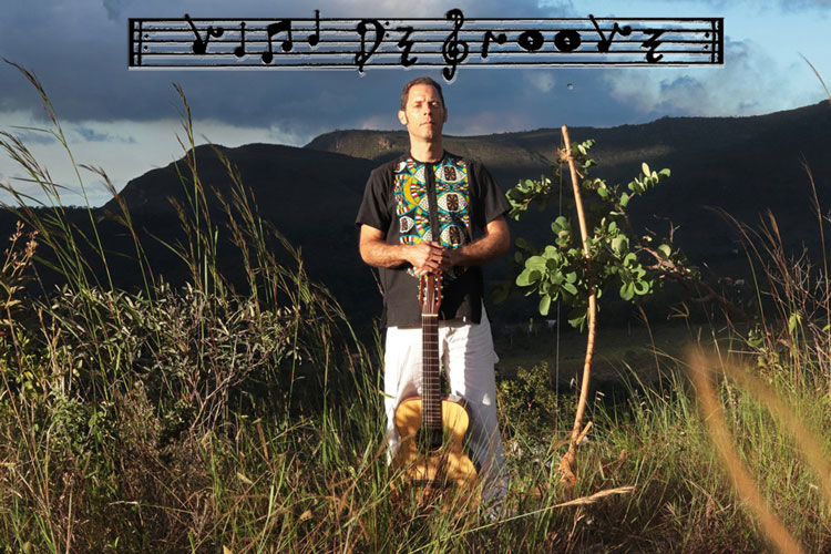 Vini De Groove in a field holding his guitar upright