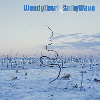 The album cover for Standing Wave by Wendy Stewart features a wintry landscape under a pale blue sky. Leafless branches and frozen ground stretch across the scene, dominated by a tall, twisting stick or reed curving upward at the center. The title and artist’s name appear in blue text at the top.