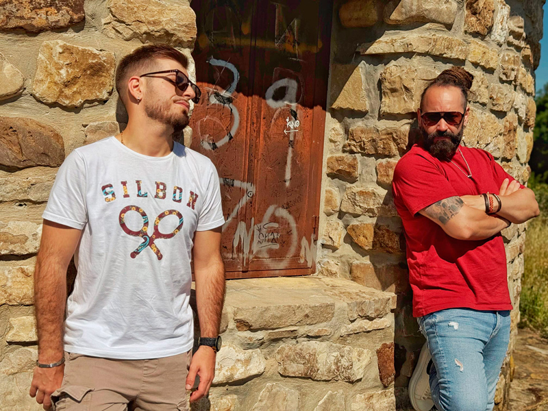 Radio Macandé. Band photo. The duo leaning against a stone wall.