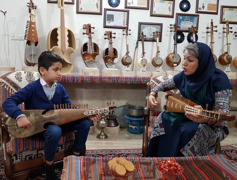 A female Rubab master is teaching a child student how to keep the fret and pluck to play the notes - Photo by Shahab Nikman, Iran, 2020