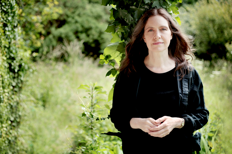 Sarah McQuaid - Photo by Phil Nicholls. The artist posing in front of a forest.